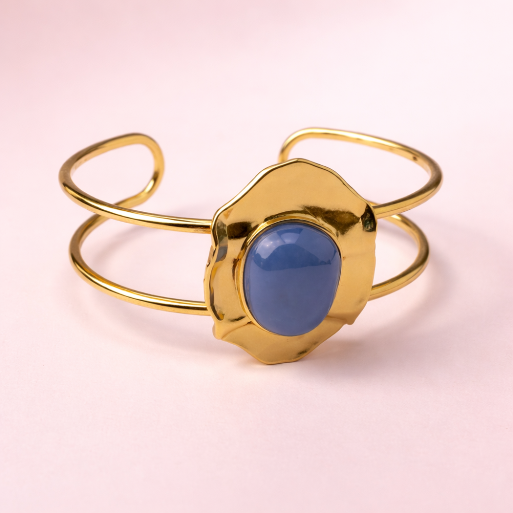 Bracelet jonc doré en acier inoxydable avec pierre bleue ovale sertie.